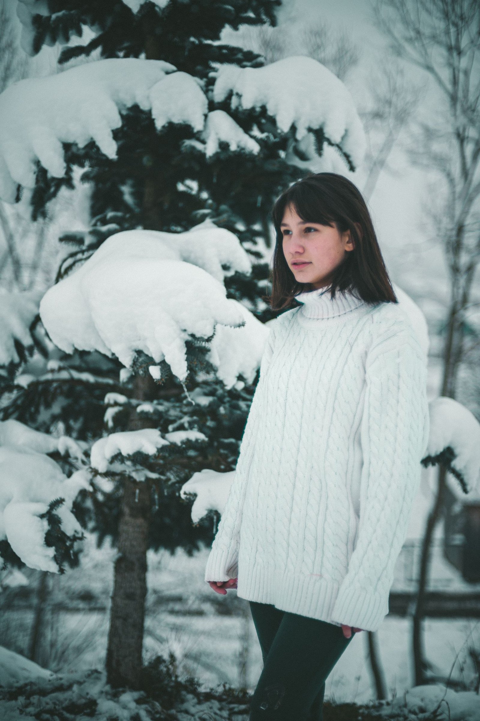 Winter quarter zip outfits - woman in a white knit sweater standing by a snow-covered tree